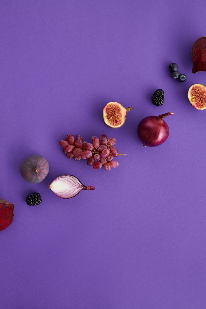 An artistic display of assorted fruits and vegetables on a purple background, perfect for healthy eating themes.